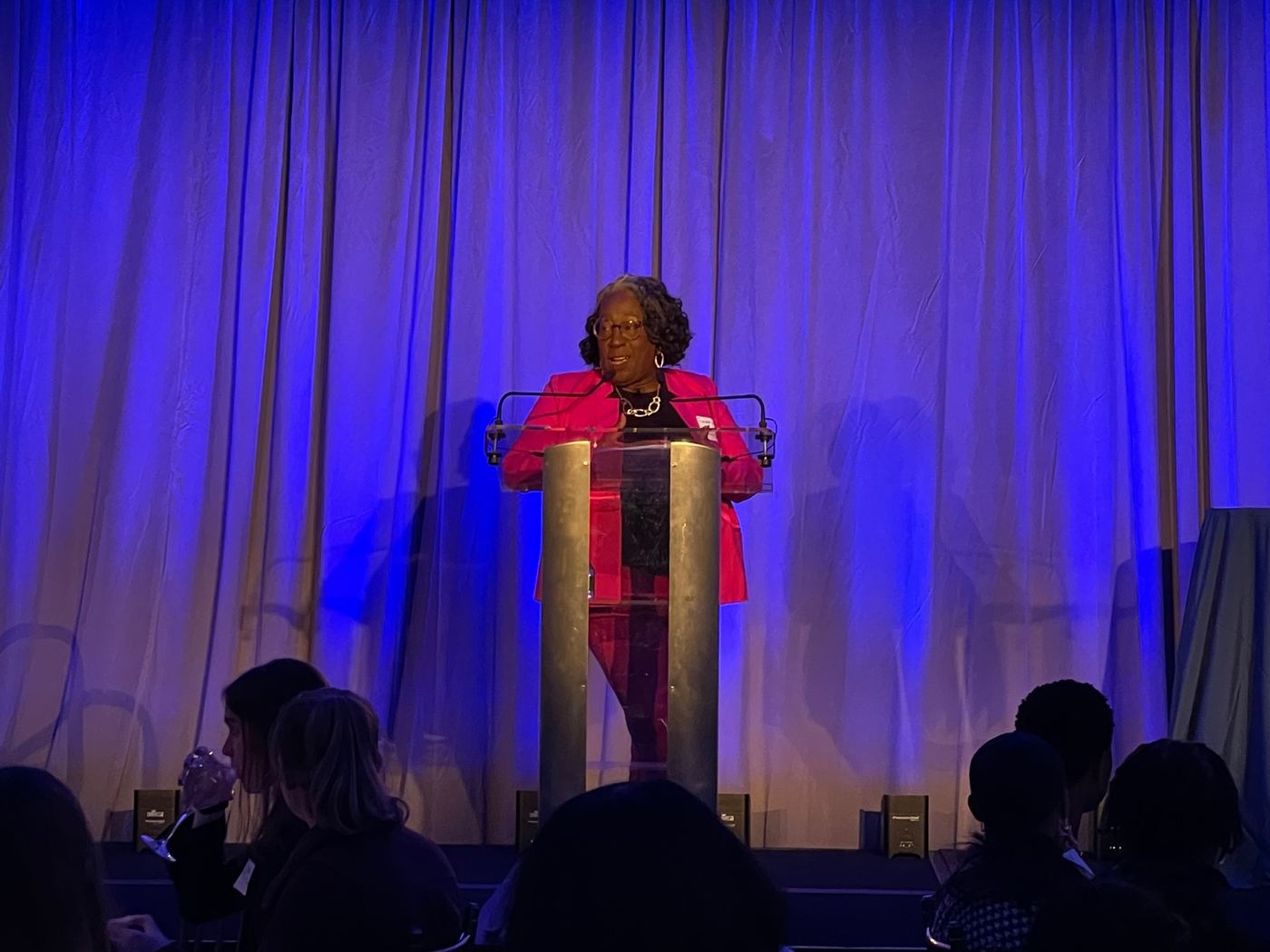 Fredericka Wallace Deena speaking from a podium to a seated audience.